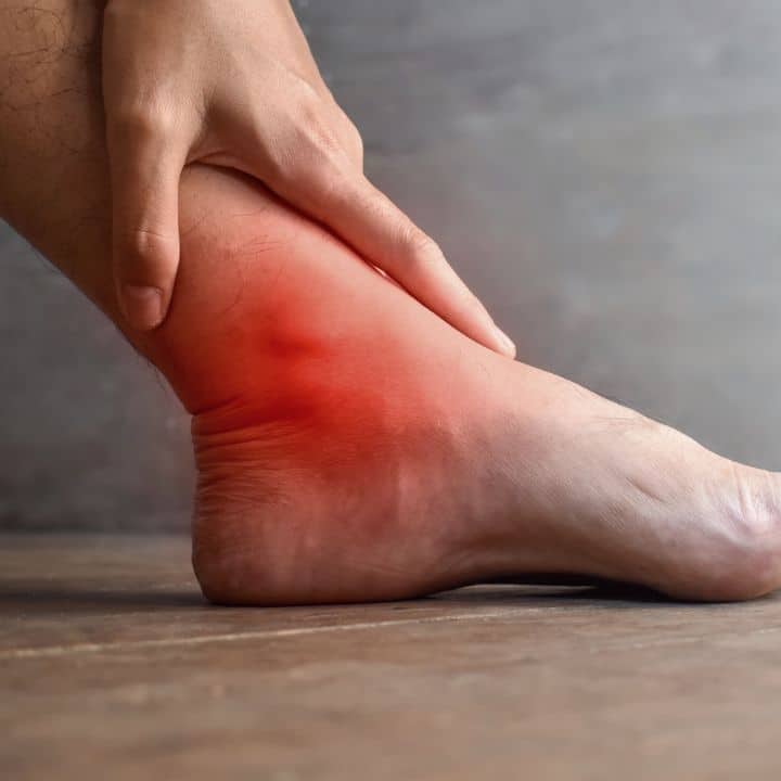 A person holding their ankle, with the painful area highlighted in red