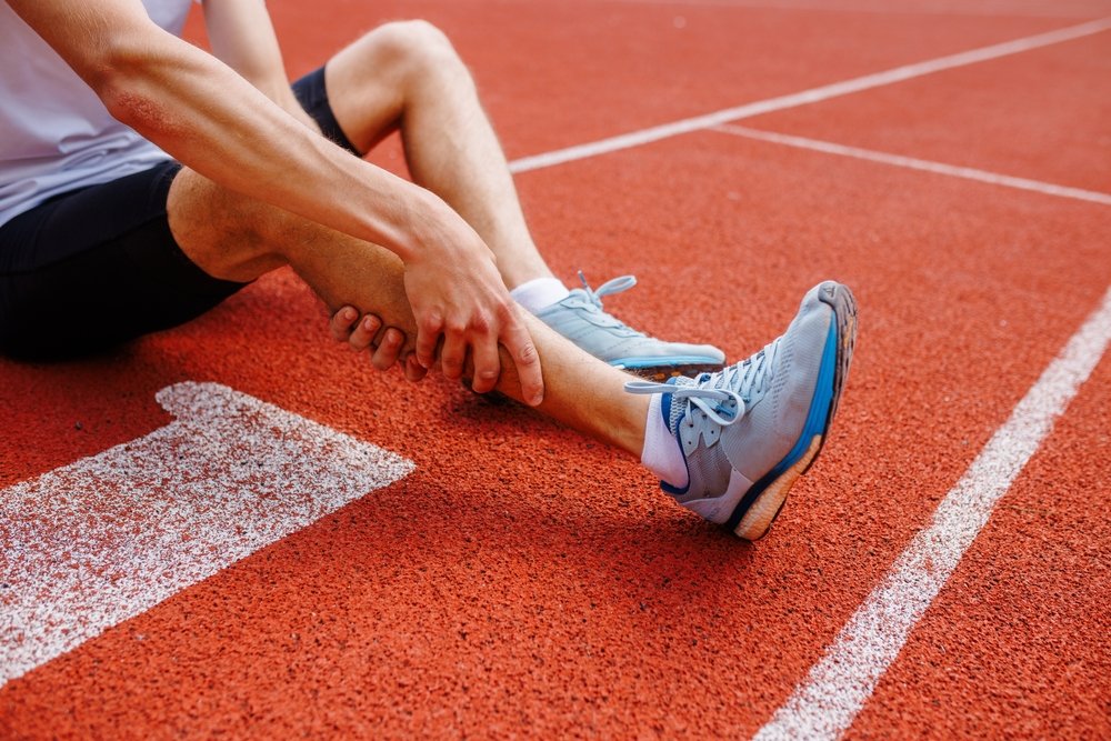 Athlete on a running track holding an injured lower leg and ankle